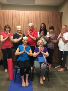 7 of our 2017-2018 season yoga participants pose for a photo, many with hands folded and yoga mats present! 