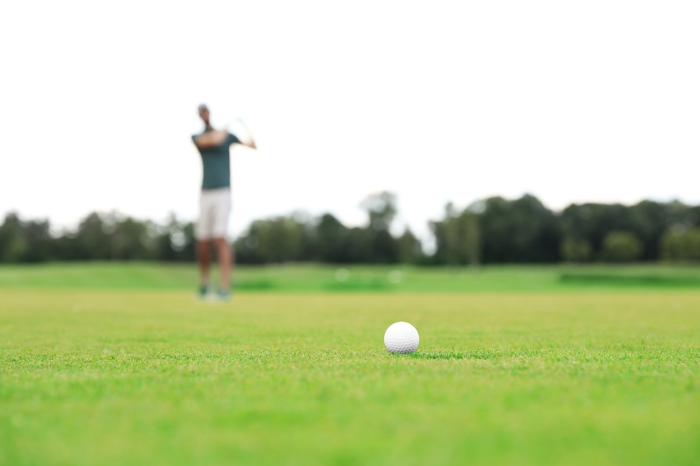 Man playing golf on green course, ball in focus. Sport and leisure